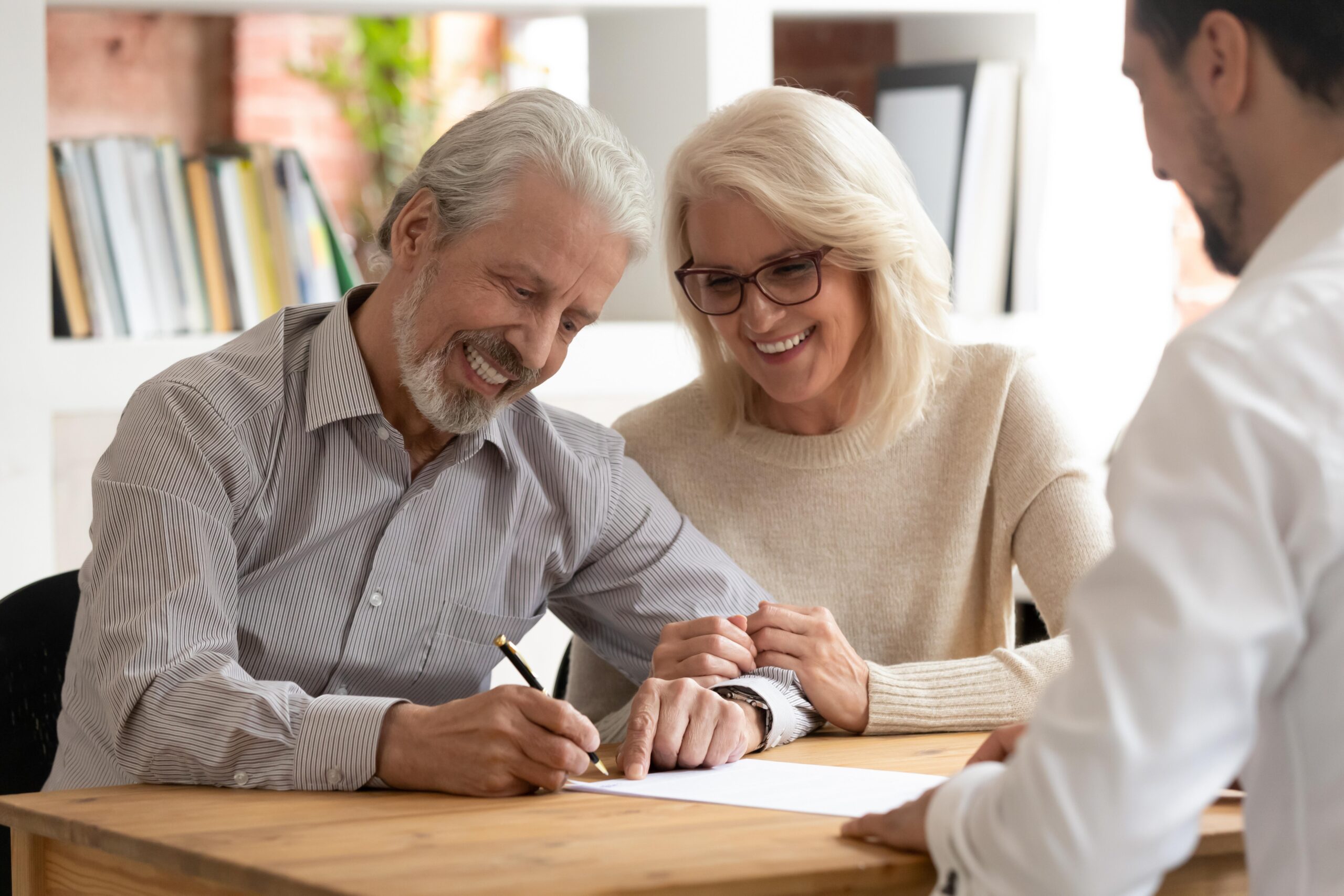 Happy older family couple clients make sale purchase deal sign insurance contract meeting estate agent lawyer bank manager, satisfied senior customers make business financial deal buy house take loan